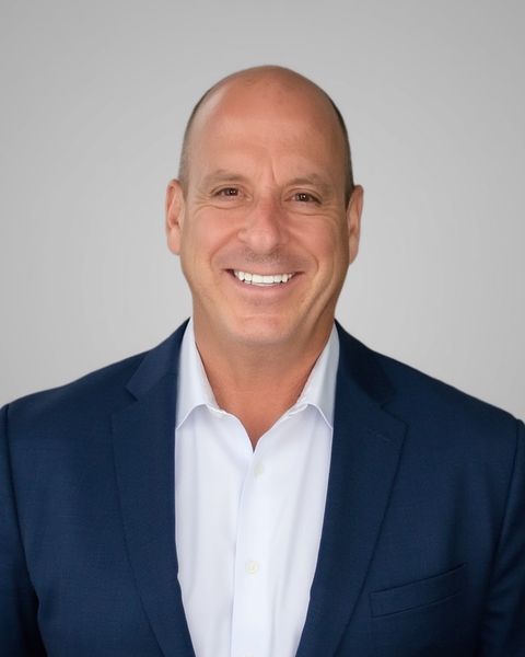 Phil Clark, smiling in a navy blazer and white shirt against a light gray background